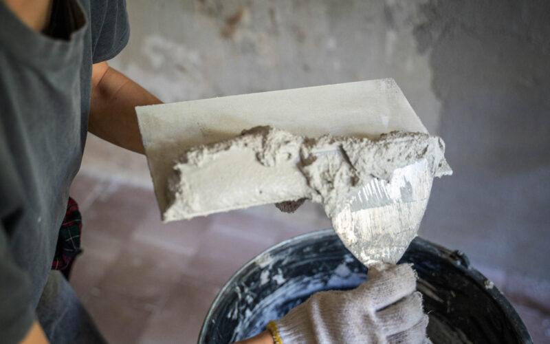 Fasadepuss | Flislegging | Ålgård mur og flis A gloved hand adds plaster to a trowel using a trowel, close-up.